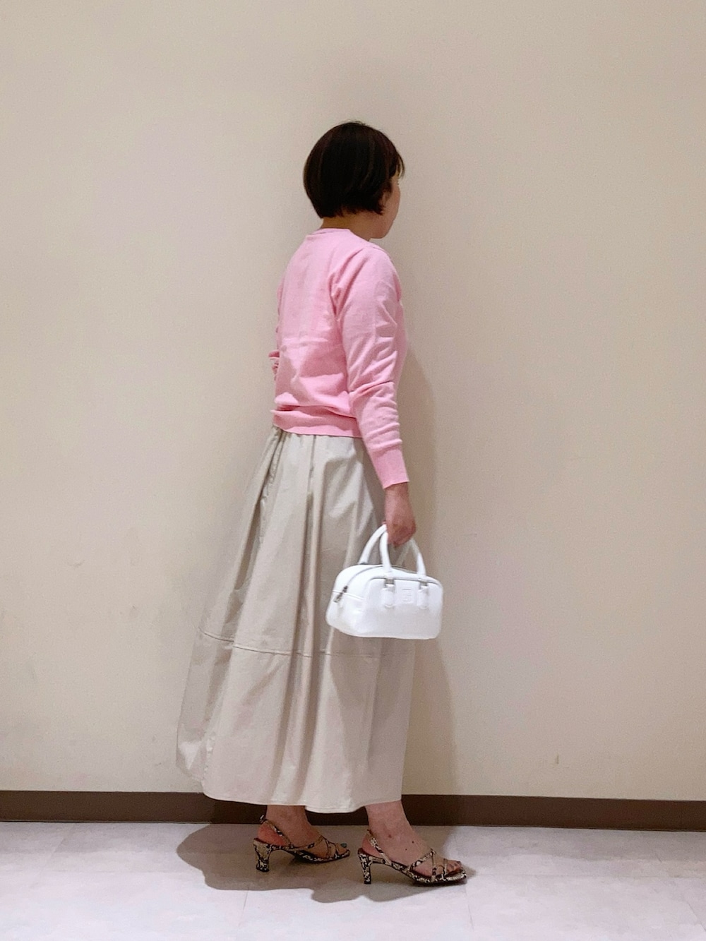 ピンク系のカーディガン/ボレロ、ベージュ系のスカート、ホワイト系のハンドバッグを着用したレディースの春コーディネートの2枚目の写真