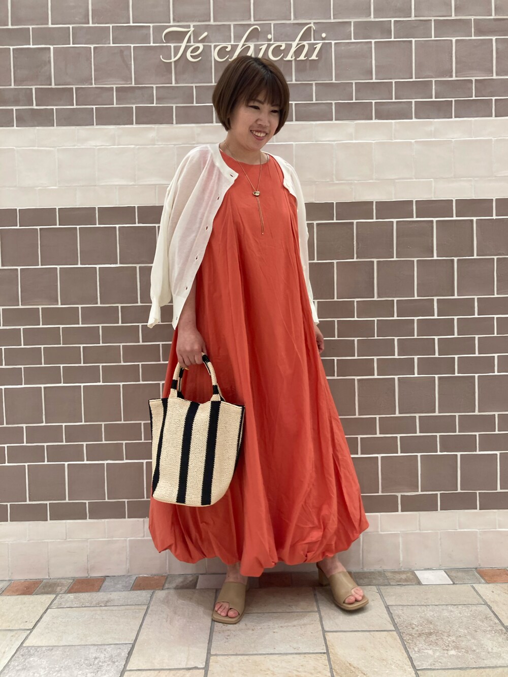ホワイト系のカーディガン/ボレロ、オレンジ系のワンピース/ドレス、ベージュ系のハンドバッグを着用したレディースの春コーディネートの2枚目の写真
