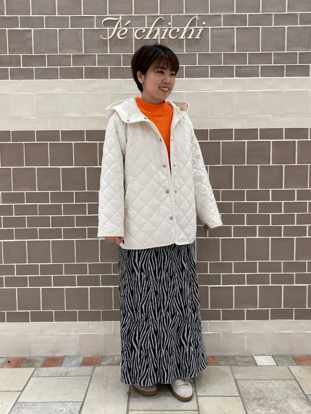 オレンジ系のニット/セーター、ホワイト系のその他アウター、ブラック系のスカートを着用したレディースの冬コーディネートの2枚目の写真