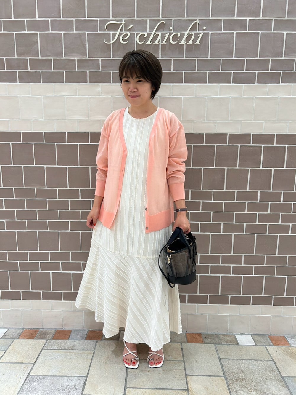 ホワイト系のワンピース、ピンク系のカーディガン/ボレロ、ホワイト系のサンダルを着用したレディースの夏コーディネートの2枚目の写真