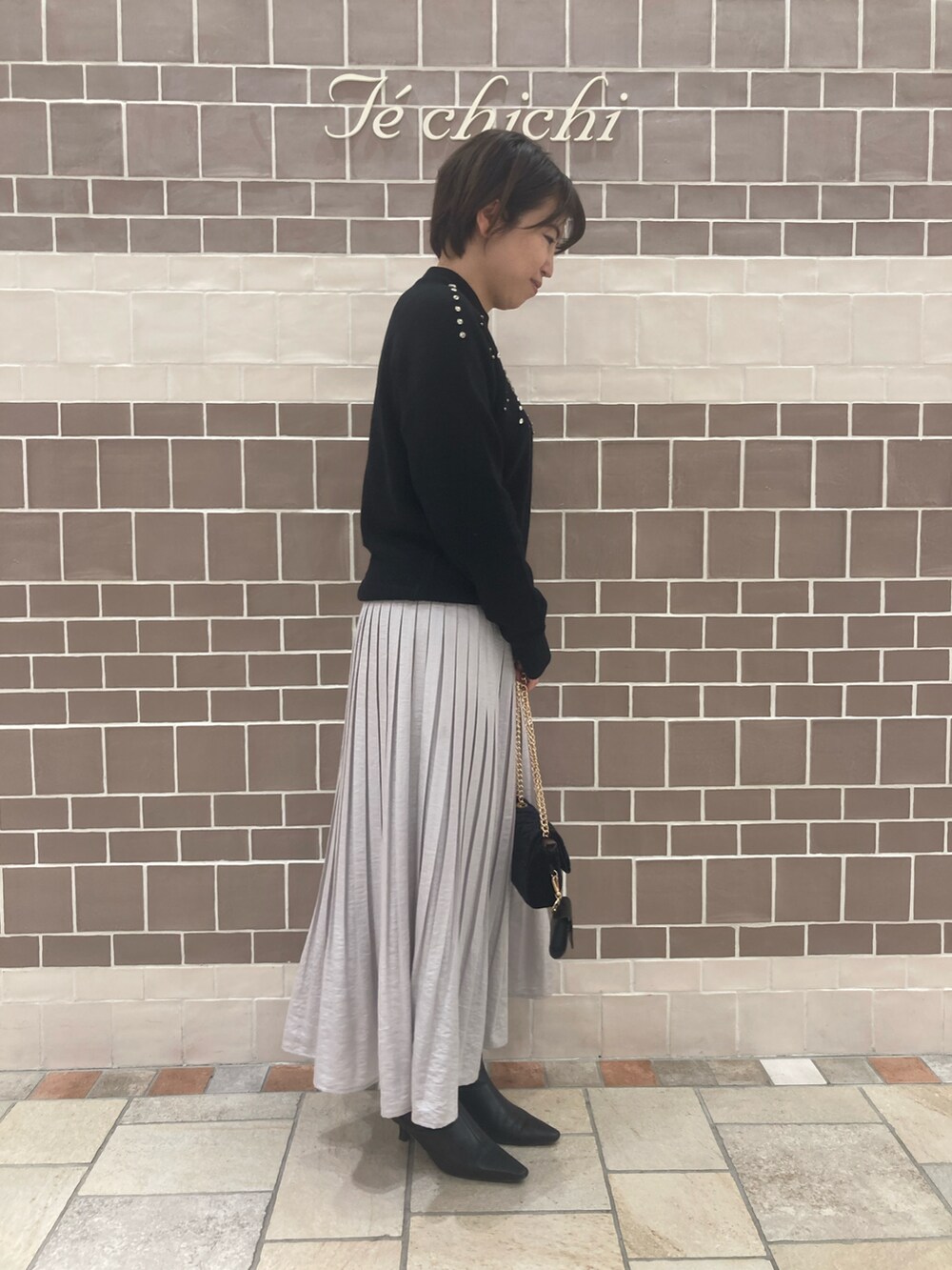 ブラック系のニット/セーター、グレー系のスカート、ブラック系のブーツを着用したレディースの秋コーディネートの2枚目の写真