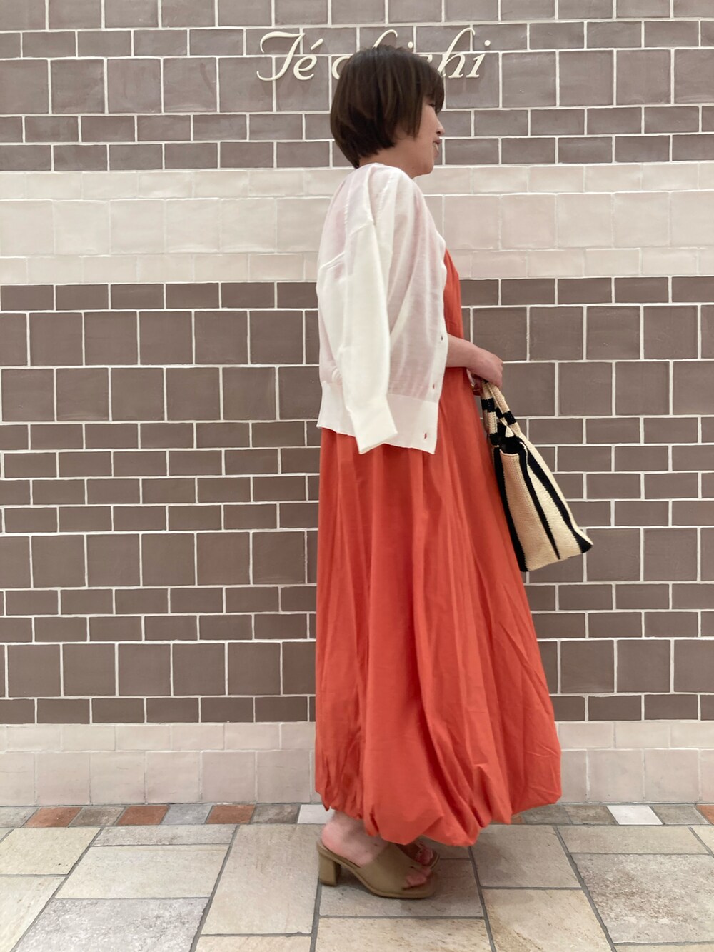 ホワイト系のカーディガン/ボレロ、オレンジ系のワンピース/ドレス、ベージュ系のハンドバッグを着用したレディースの春コーディネートの3枚目の写真
