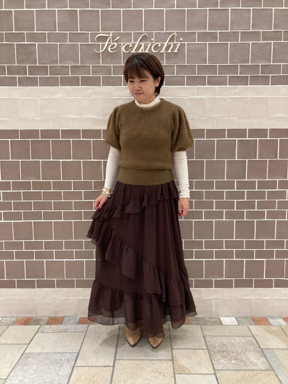 ブラウン系のニット/セーター、ブラウン系のスカート、ホワイト系のTシャツ/カットソーを着用したレディースの秋コーディネートの2枚目の写真