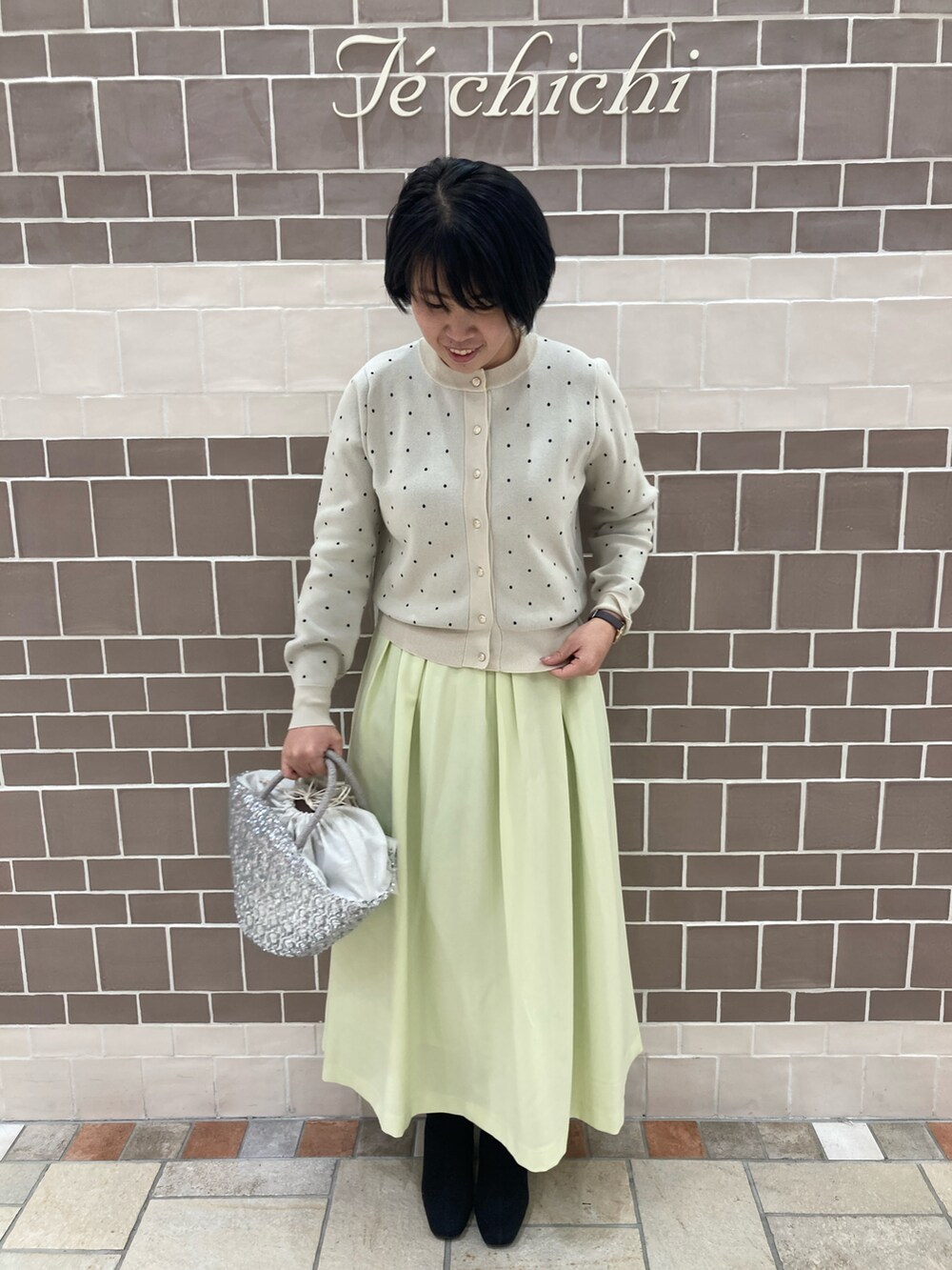 ホワイト系のカーディガン/ボレロ、イエロー系のスカート、シルバー系のハンドバッグを着用したレディースの冬コーディネートの2枚目の写真