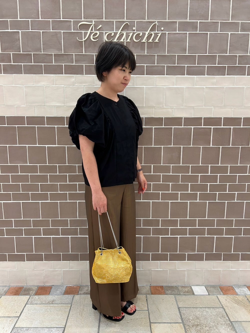 ブラック系のシャツ/ブラウス、ブラウン系のパンツ、ゴールド系のハンドバッグを着用したレディースの夏コーディネートの2枚目の写真