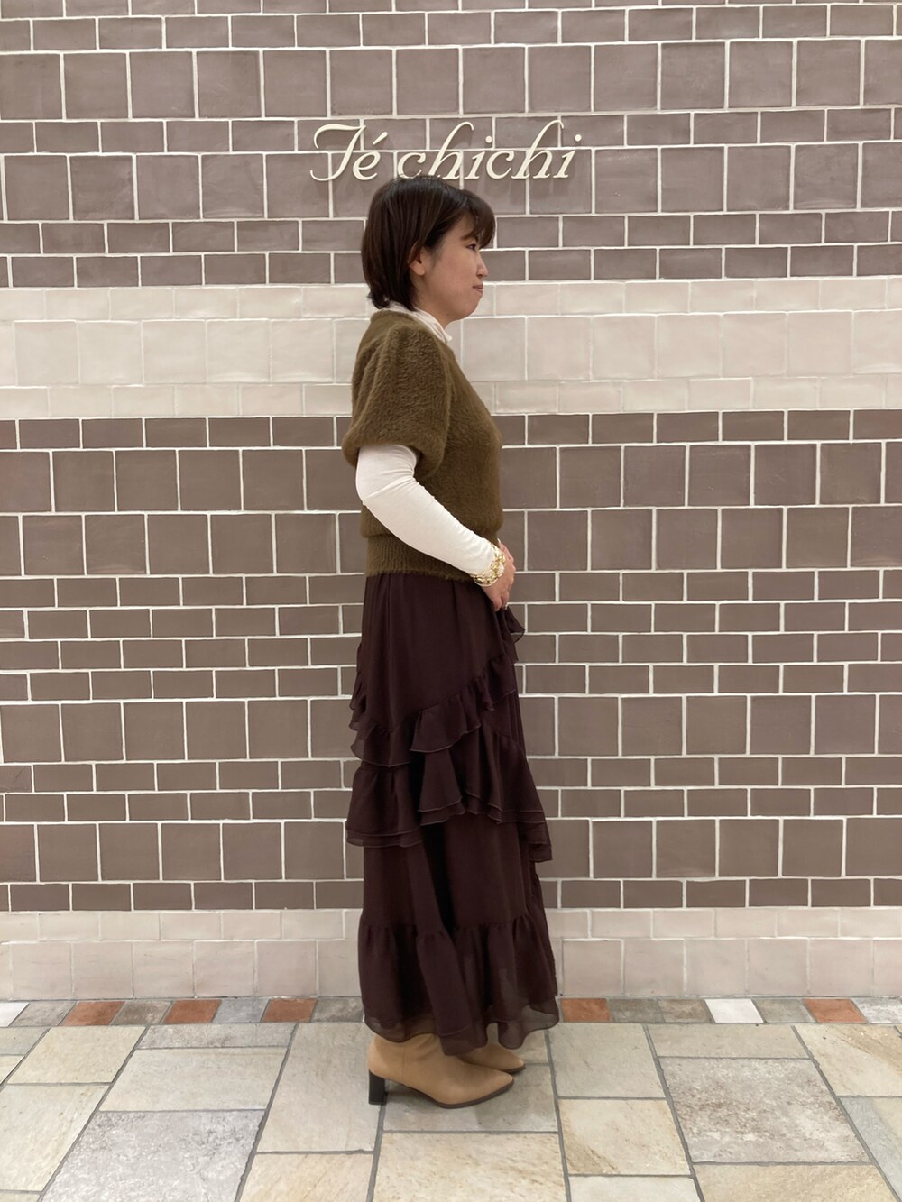 ブラウン系のニット/セーター、ブラウン系のスカート、ホワイト系のTシャツ/カットソーを着用したレディースの秋コーディネートの3枚目の写真