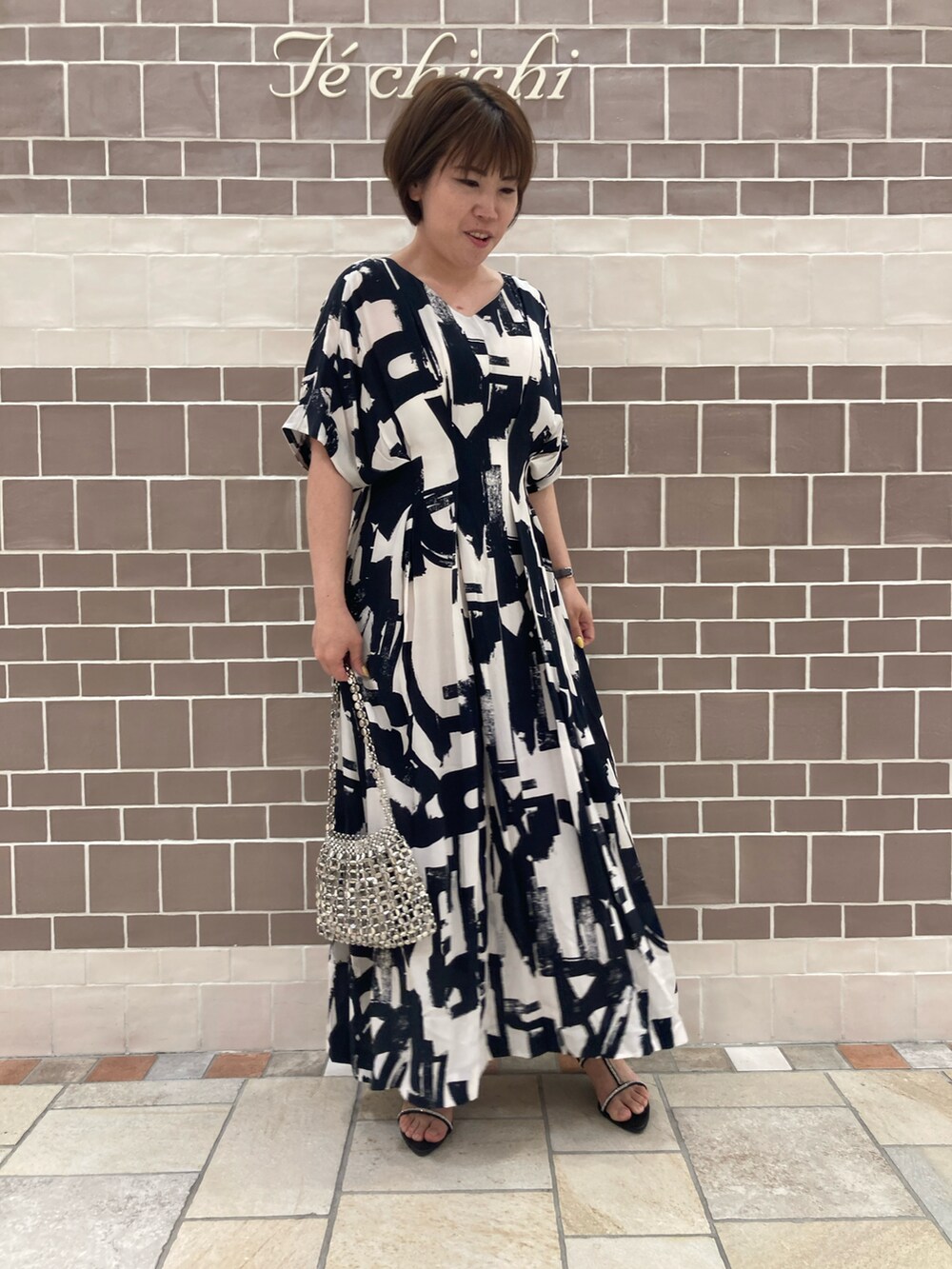 ブラック系のワンピース/ドレス、シルバー系のハンドバッグ、ブラック系のサンダルを着用したレディースの春コーディネートの2枚目の写真