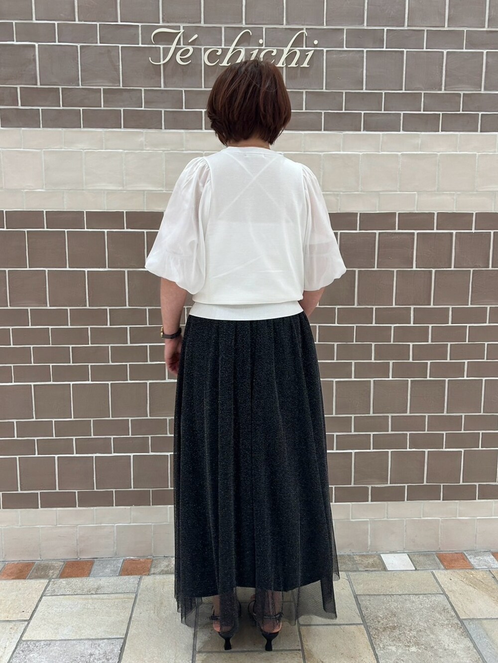 ホワイト系のニット/セーター、ブラック系のスカート、ブラック系のサンダルを着用したレディースの春コーディネートの4枚目の写真