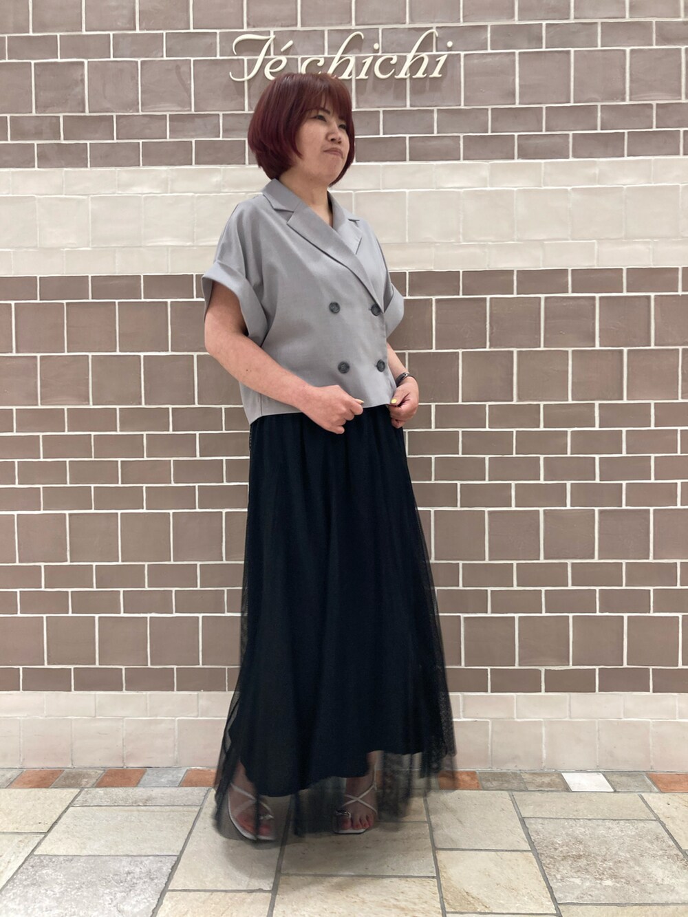 グレー系のノーカラージャケット、ブラック系のスカート、ホワイト系のサンダルを着用したレディースの夏コーディネートの2枚目の写真