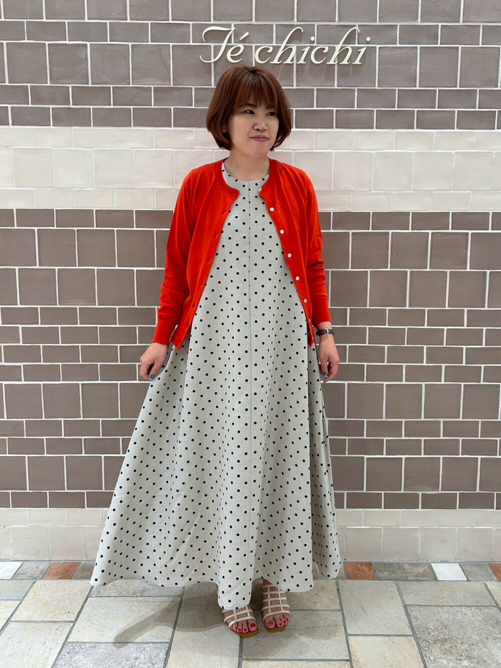 ベージュ系のワンピース/ドレス、レッド系のカーディガン/ボレロ、ホワイト系のサンダルを着用したレディースの夏コーディネートの2枚目の写真