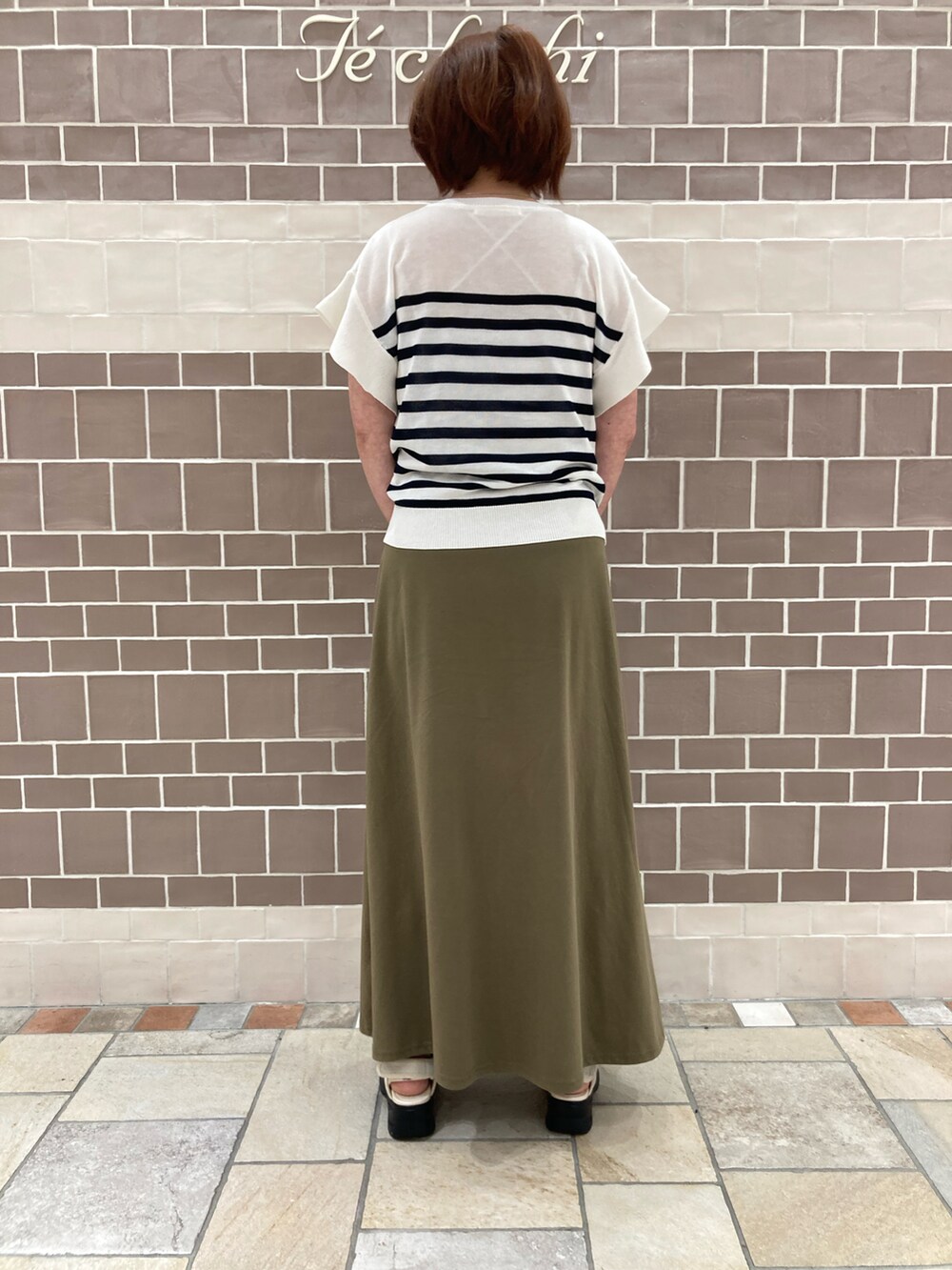 グレー系のハンドバッグ、ホワイト系のニット/セーター、グリーン系のスカートを着用したレディースの夏コーディネートの3枚目の写真