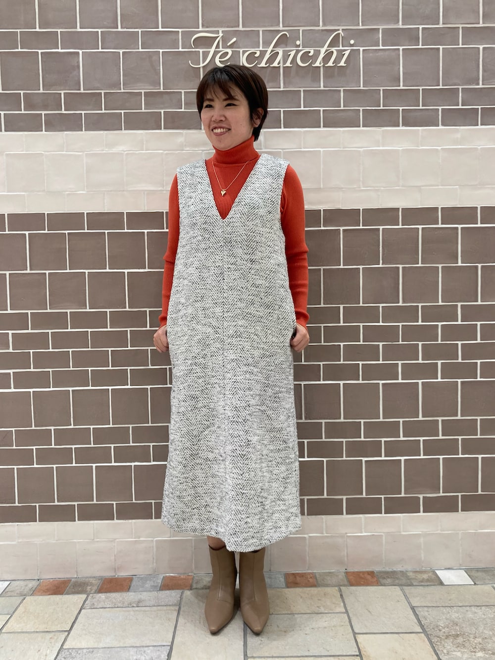 オレンジ系のニット/セーター、グレー系のその他アウターを着用したレディースの冬コーディネートの2枚目の写真