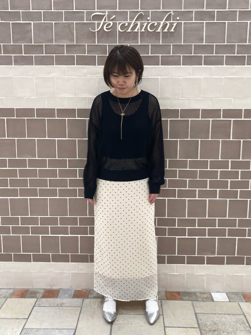 ブラック系のニット/セーター、ベージュ系のスカート、シルバー系のパンプスを着用したレディースの春コーディネートの2枚目の写真