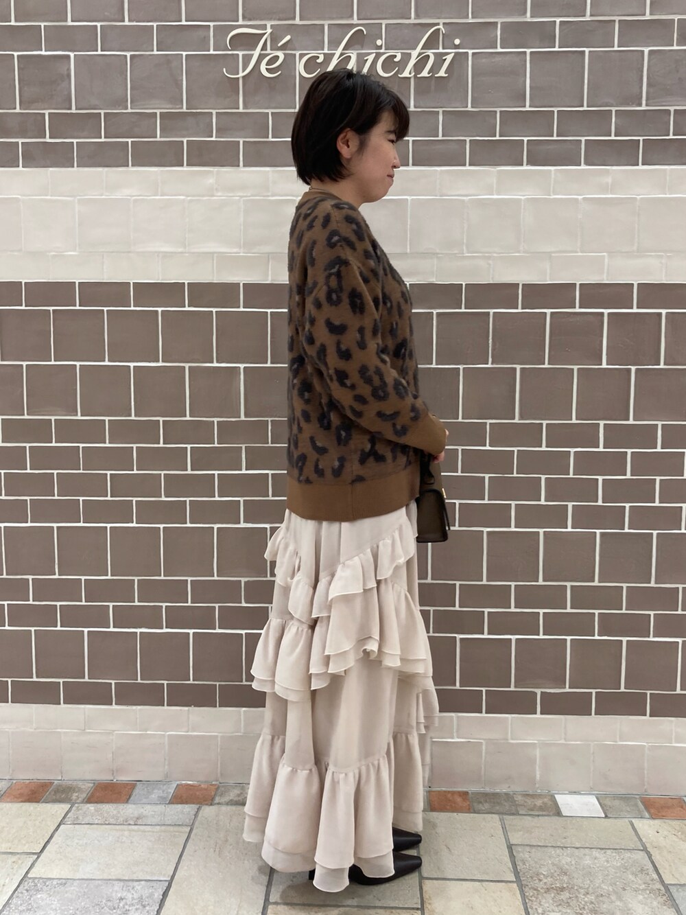 ブラウン系のニット/セーター、ベージュ系のスカート、ブラウン系のブーツを着用したレディースの秋コーディネートの2枚目の写真