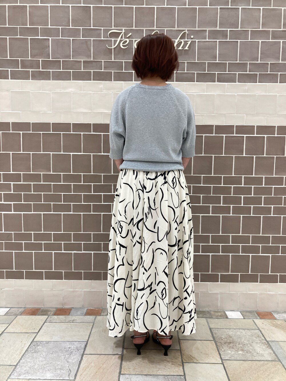 シルバー系のニット/セーター、ホワイト系のスカート、ブラック系のハンドバッグを着用したレディースの夏コーディネートの3枚目の写真