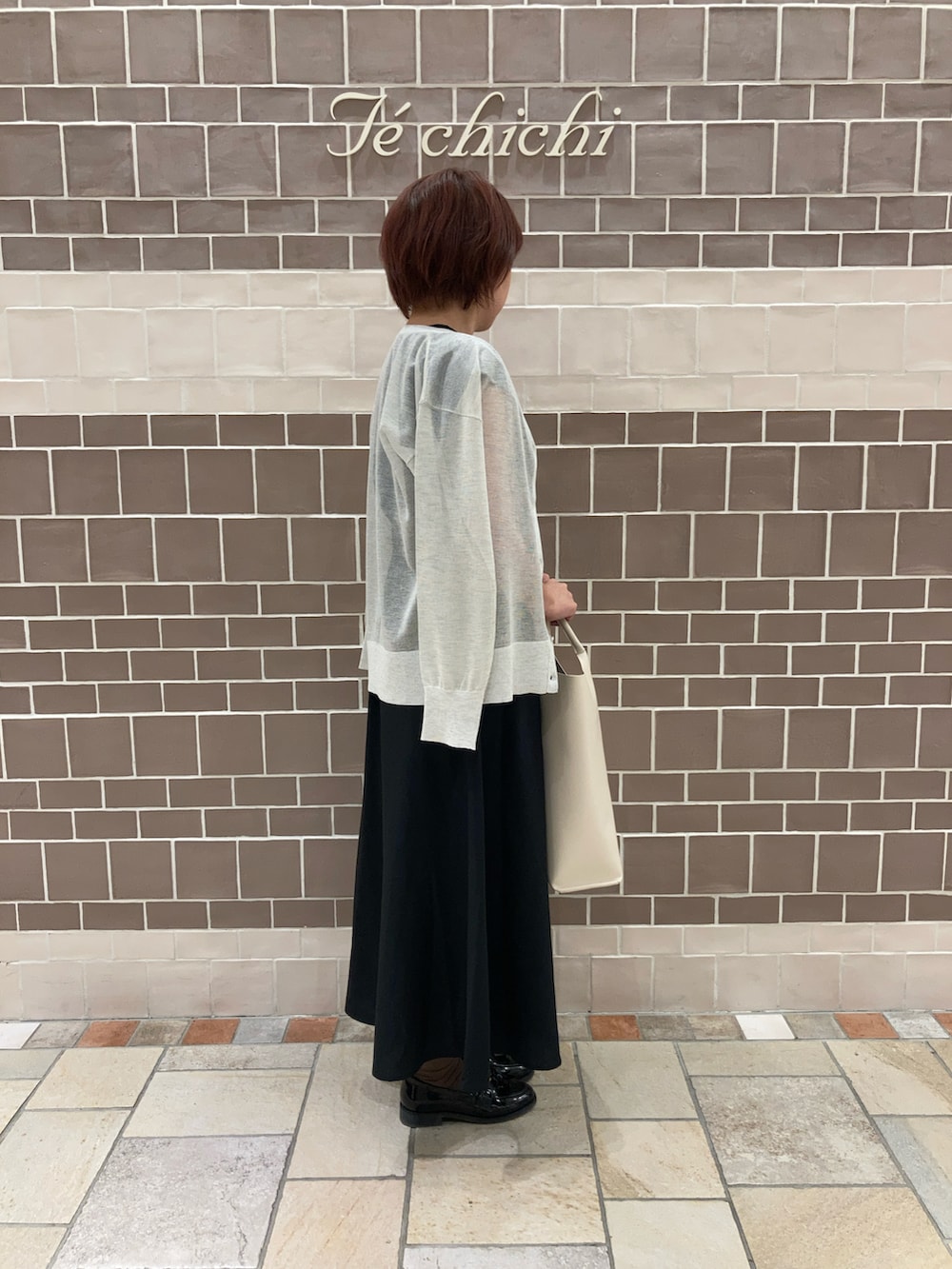 ブラック系のワンピース、ホワイト系のハンドバッグ、グレー系のカーディガン/ボレロを着用したレディースの夏コーディネートの2枚目の写真