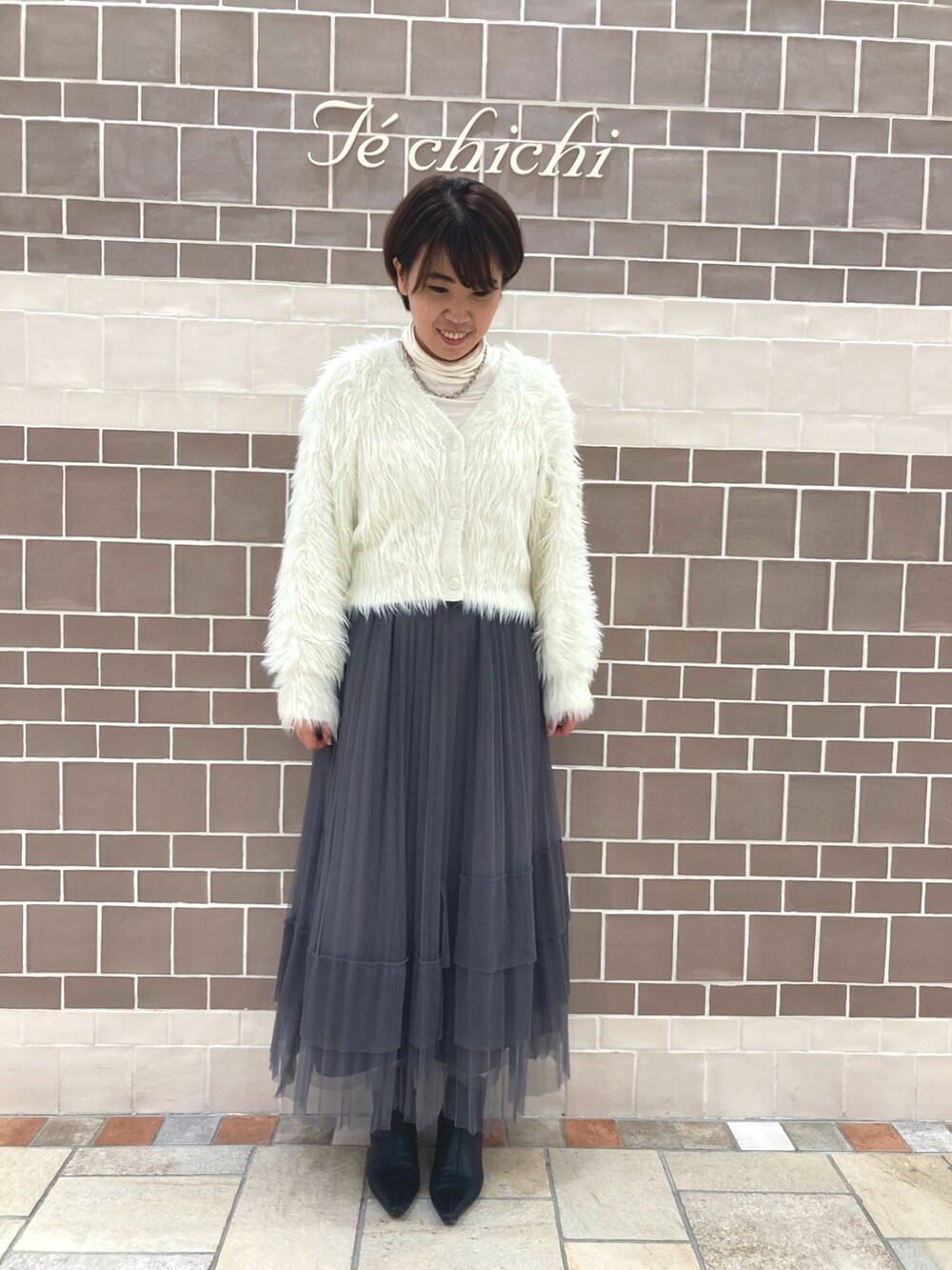 ホワイト系のニット/セーター、グレー系のスカート、ホワイト系のTシャツ/カットソーを着用したレディースの秋コーディネートの2枚目の写真