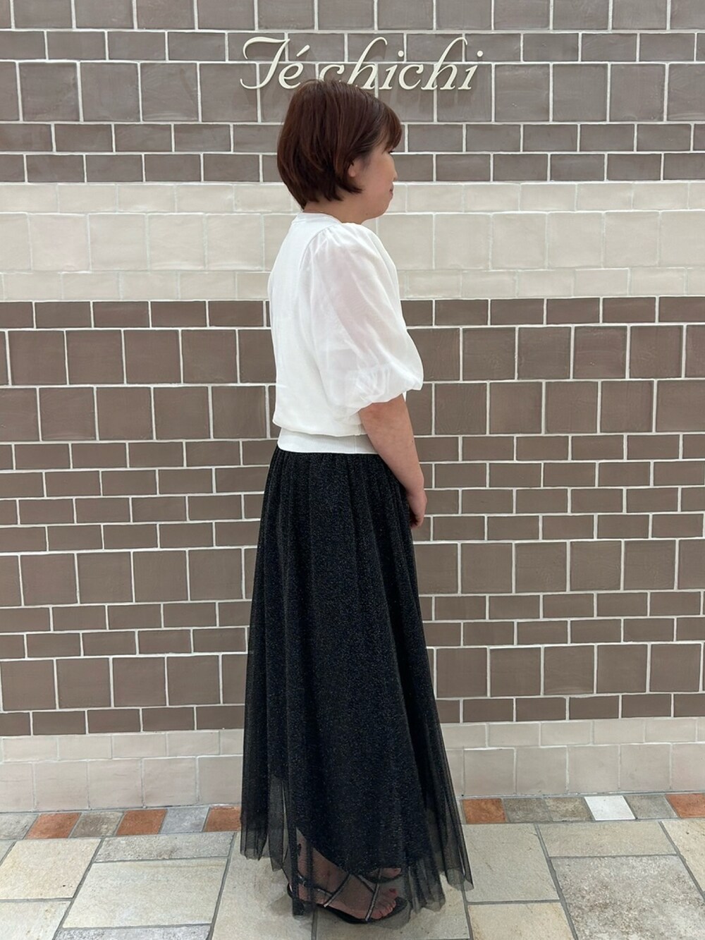 ホワイト系のニット/セーター、ブラック系のスカート、ブラック系のサンダルを着用したレディースの春コーディネートの3枚目の写真