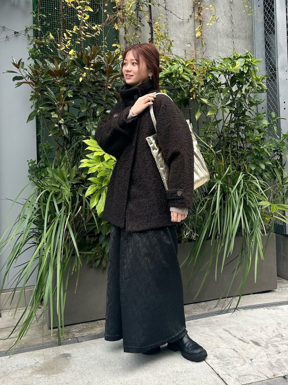 ゴールド系のトートバッグ、ブラウン系のステンカラーコート、ブラック系のワンピースを着用したレディースの冬コーディネートの3枚目の写真