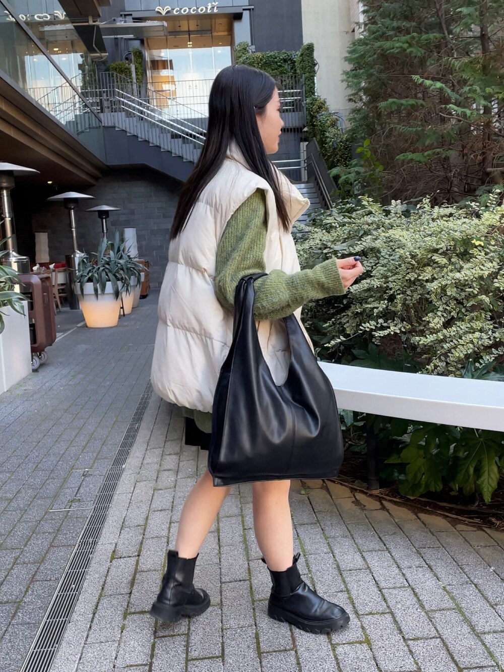 ブラック系のトートバッグ、ホワイト系のダウンベスト、グリーン系のニット/セーターを着用したレディースの冬コーディネートの2枚目の写真