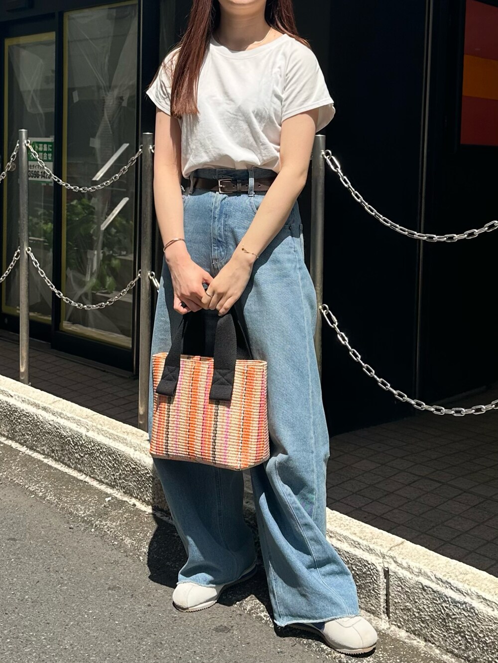 オレンジ系のトートバッグ、ホワイト系のTシャツ/カットソー、ブルー系のデニムパンツを着用したレディースの春コーディネートの2枚目の写真