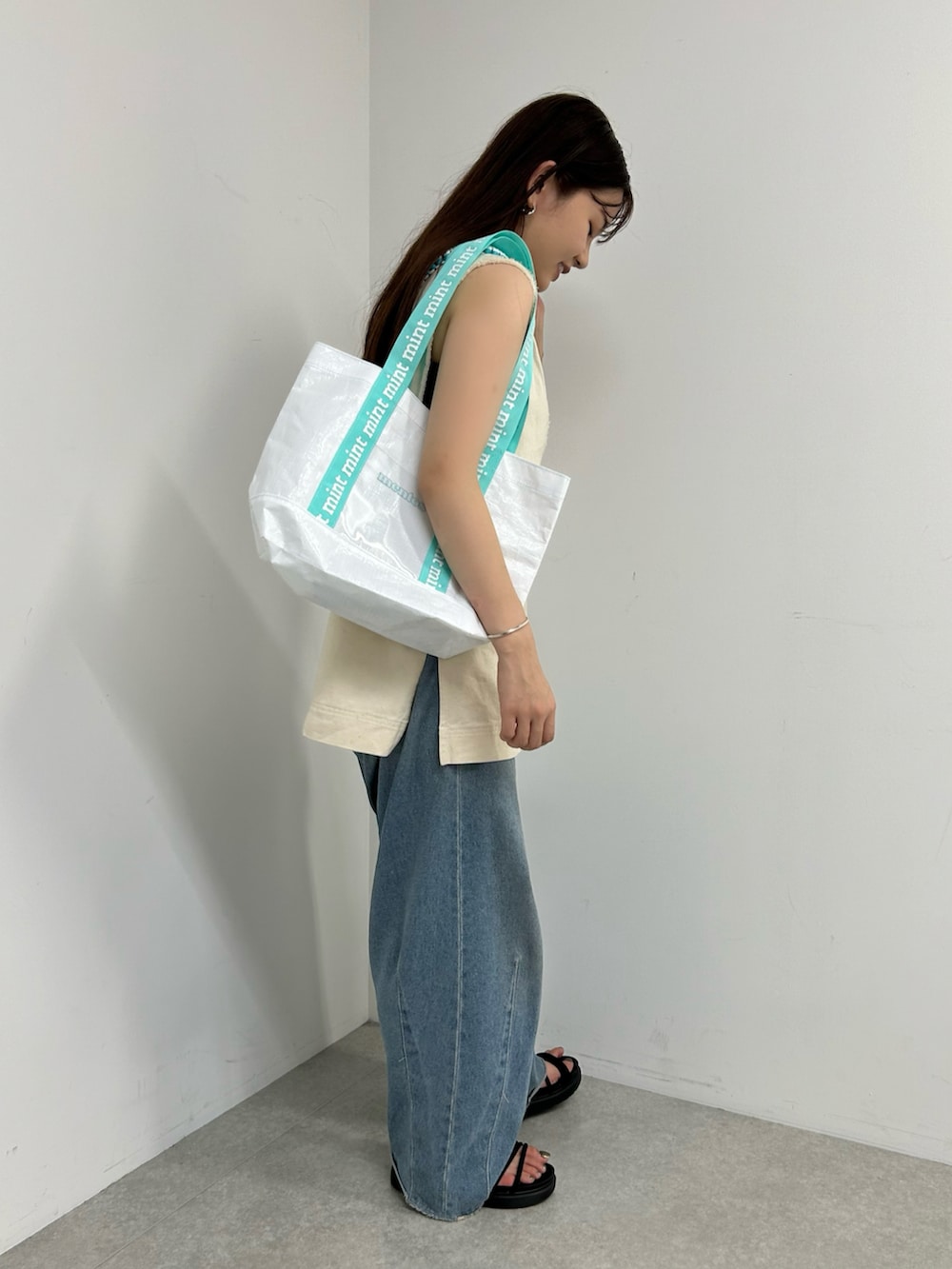 ブルー系のトートバッグ、ホワイト系のベスト、ブルー系のデニムパンツを着用したレディースの夏コーディネートの3枚目の写真