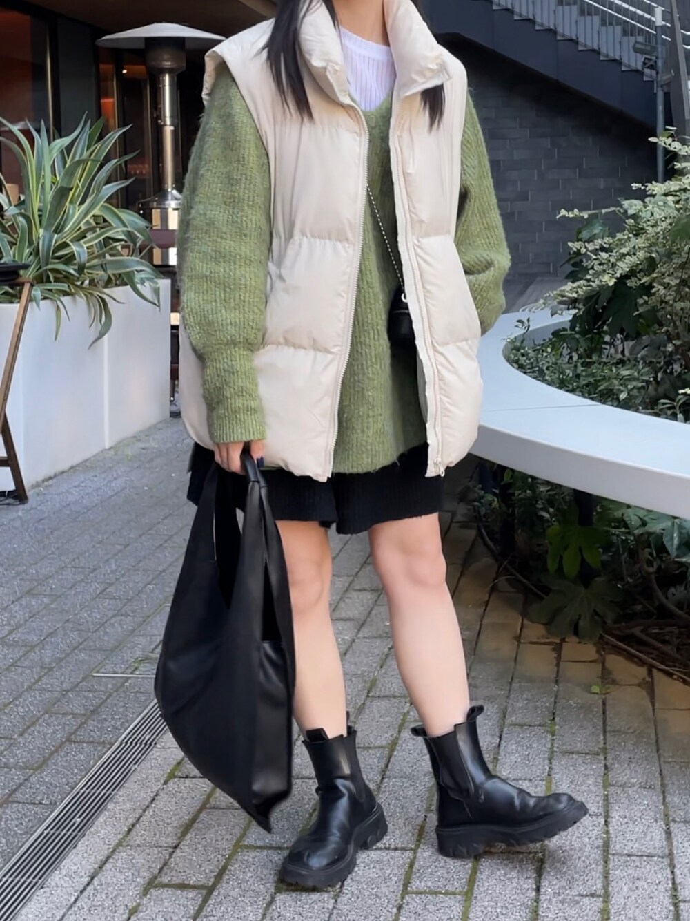 ブラック系のトートバッグ、ホワイト系のダウンベスト、グリーン系のニット/セーターを着用したレディースの冬コーディネートの3枚目の写真