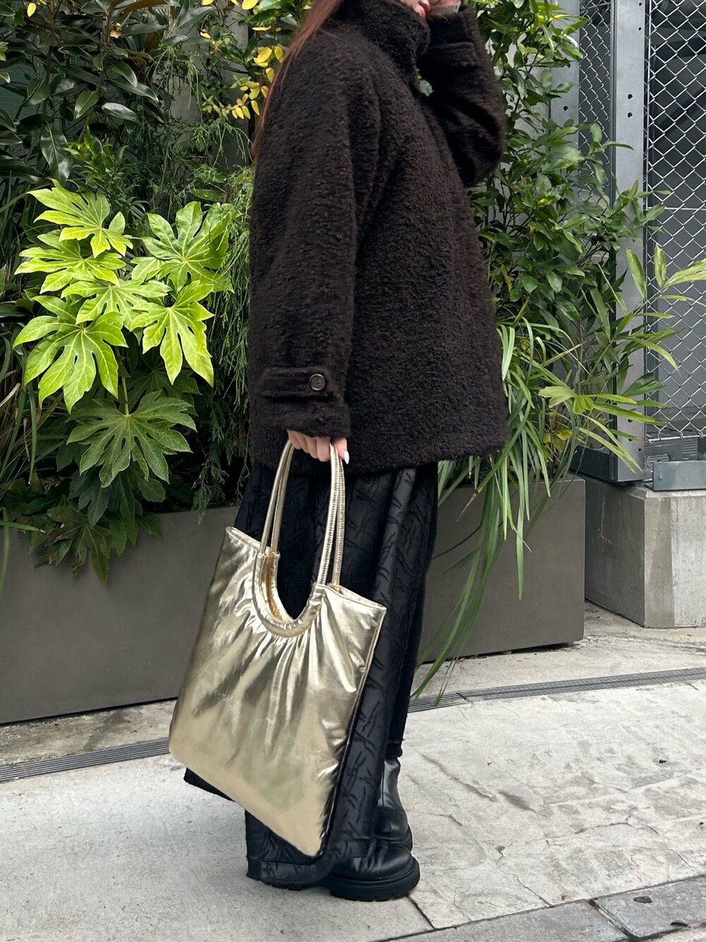 ゴールド系のトートバッグ、ブラウン系のステンカラーコート、ブラック系のワンピースを着用したレディースの冬コーディネートの2枚目の写真