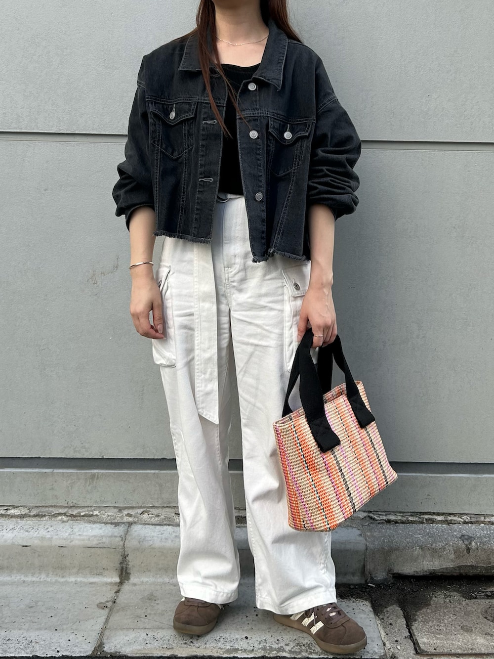 オレンジ系のトートバッグ、ブラック系のデニムジャケット、ブラック系のニット/セーターを着用したレディースの春コーディネートの2枚目の写真
