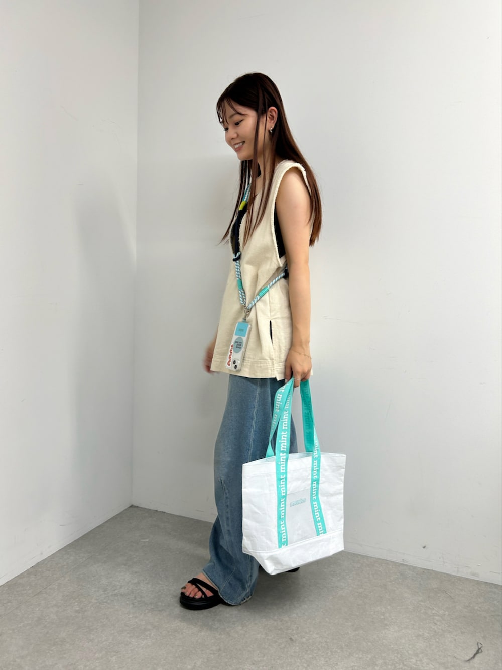 ブルー系のトートバッグ、ホワイト系のベスト、ブルー系のデニムパンツを着用したレディースの夏コーディネートの2枚目の写真