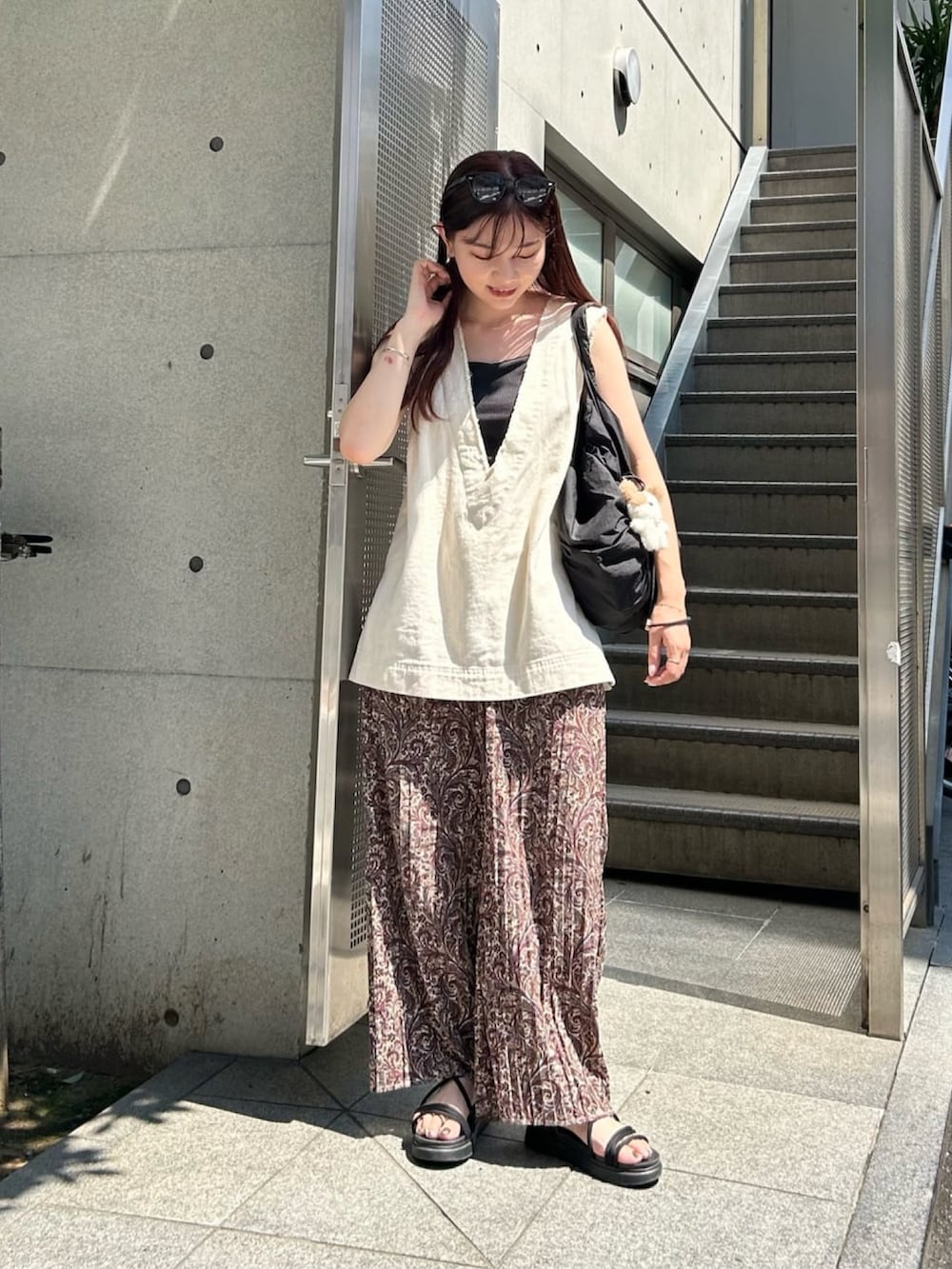 ブラック系のトートバッグ、ホワイト系のベスト、ブラウン系のその他パンツを着用したレディースの夏コーディネートの2枚目の写真