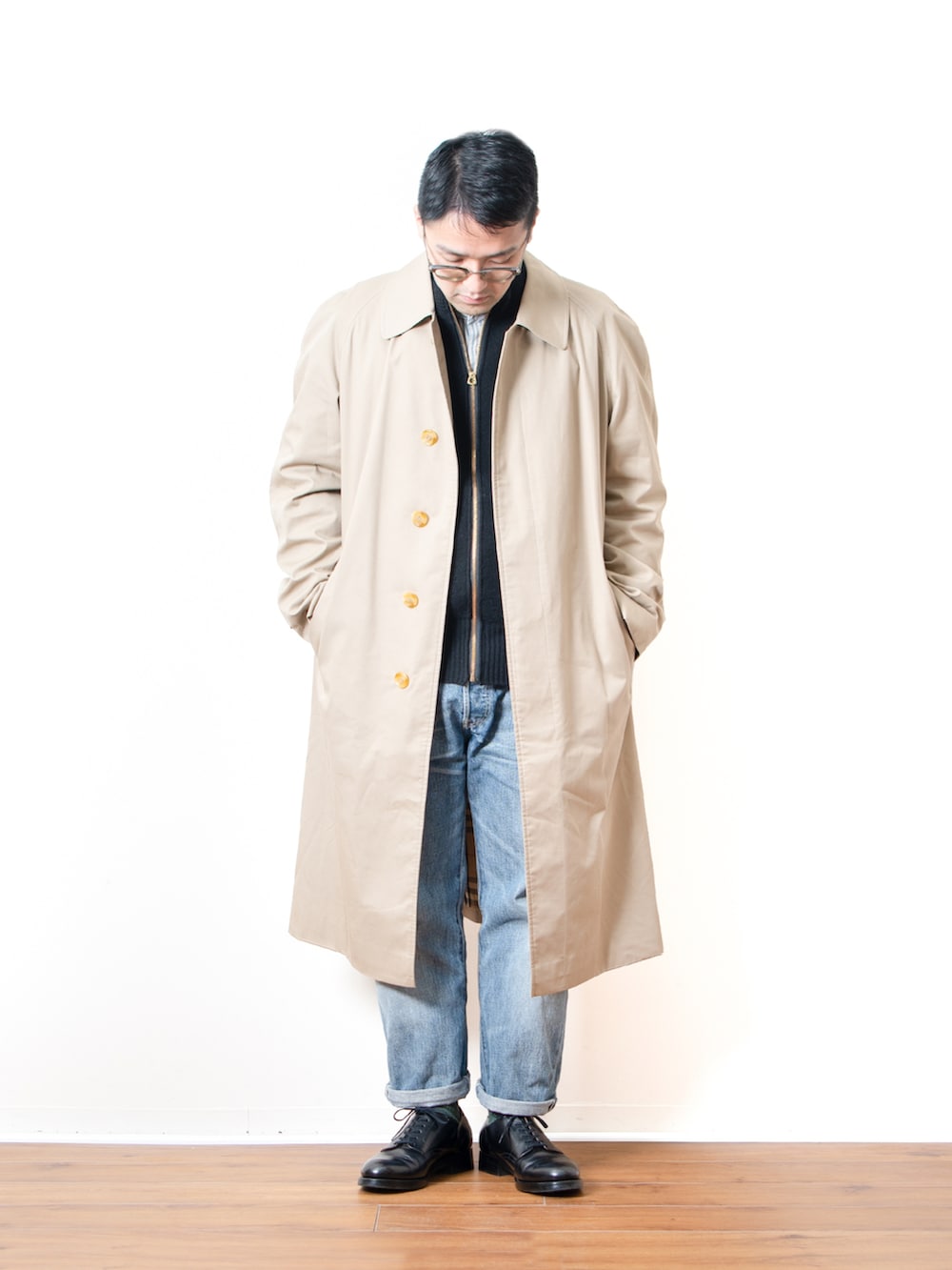 ブルー系のデニムパンツ、ブラック系のニット/セーター、ベージュ系のステンカラーコートを着用したメンズの春コーディネートの2枚目の写真