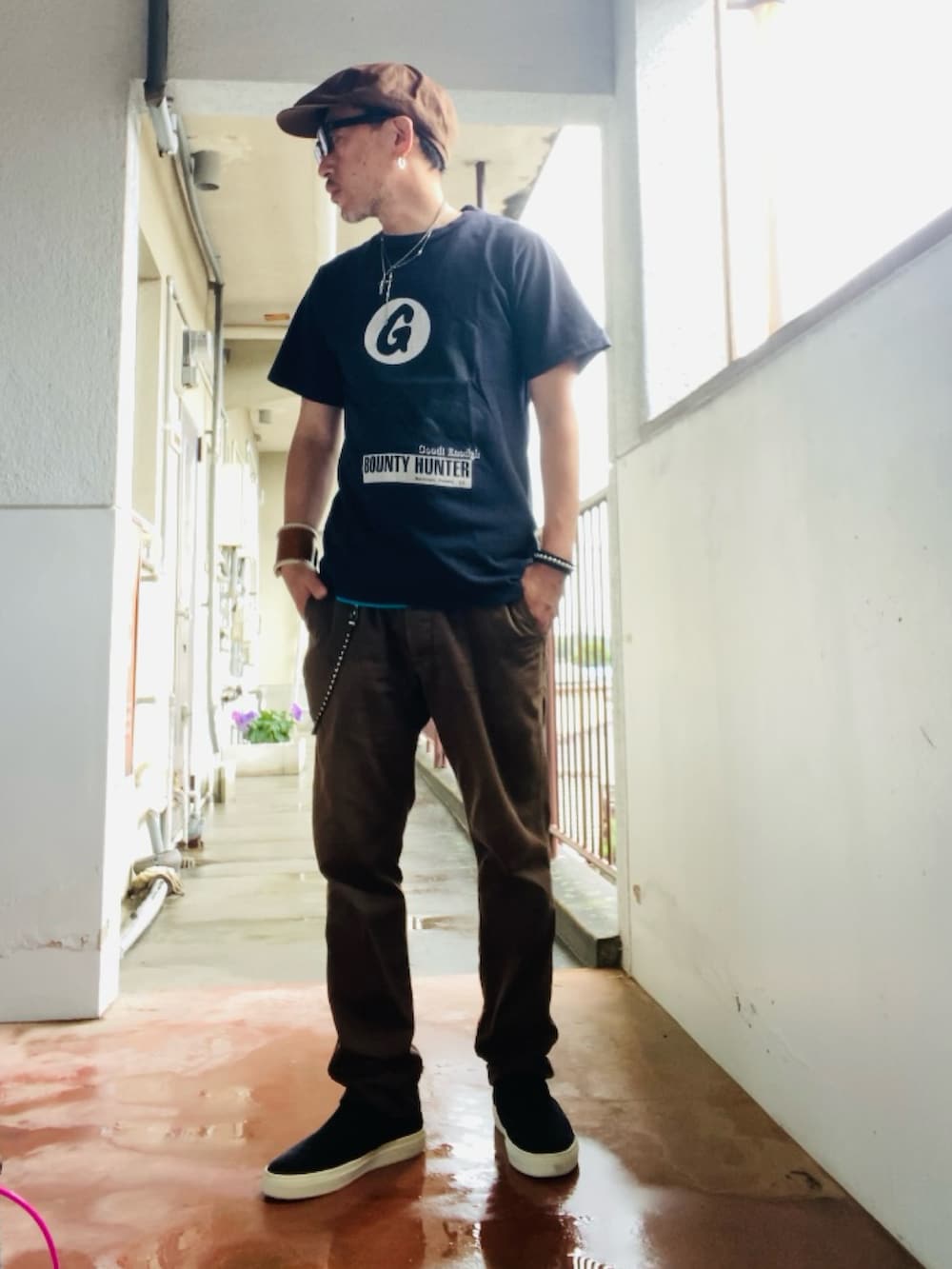 ブラウン系のチノパンツ、ブラック系のTシャツ/カットソー、ブラック系のスリッポンを着用したメンズの夏コーディネートの4枚目の写真