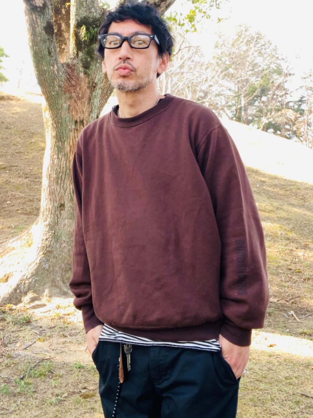 ブラック系のトップス、ブラウン系のスウェット、ブラック系のチノパンツを着用したメンズの春コーディネートの3枚目の写真