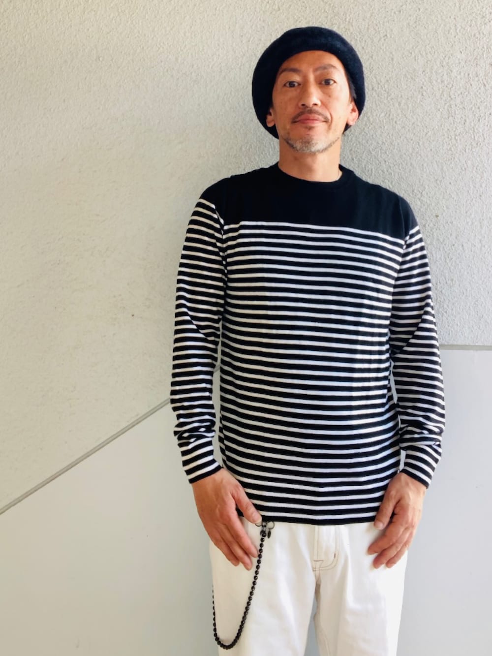 ブラック系のニット/セーター、ホワイト系のデニムパンツ、ブラック系のサンダルを着用したメンズの夏コーディネートの2枚目の写真