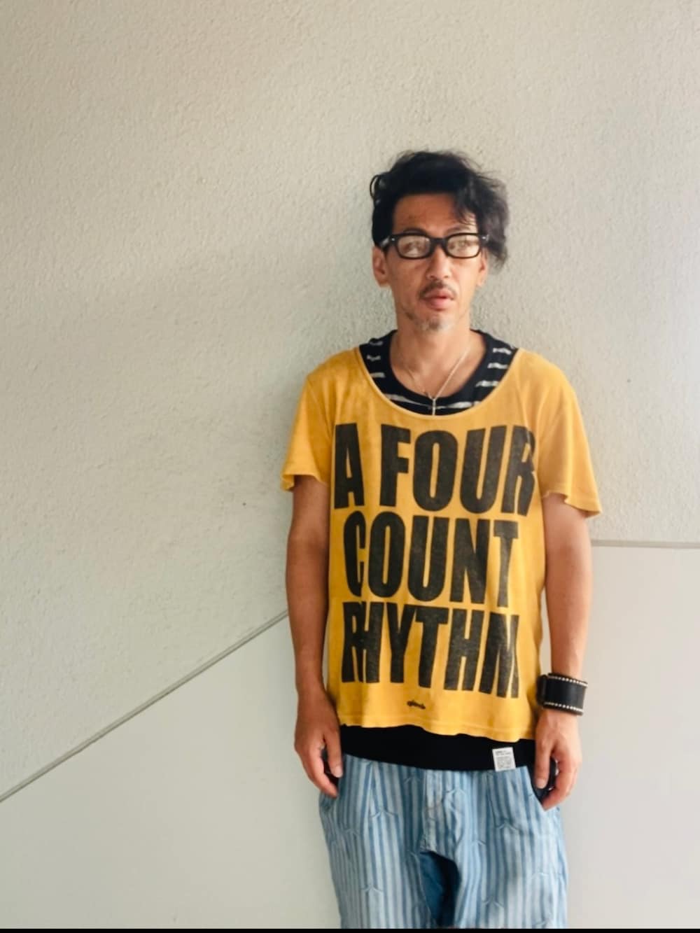 ゴールド系のTシャツ/カットソー、ブルー系のデニムパンツ、ブラック系のサンダルを着用したメンズの夏コーディネートの2枚目の写真