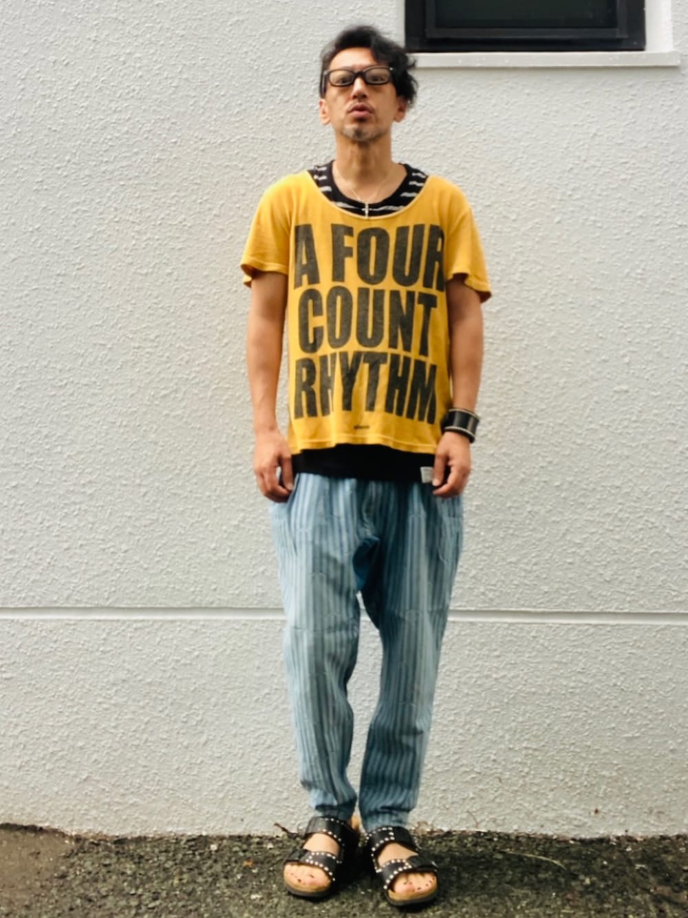 ゴールド系のTシャツ/カットソー、ブルー系のデニムパンツ、ブラック系のサンダルを着用したメンズの夏コーディネートの3枚目の写真