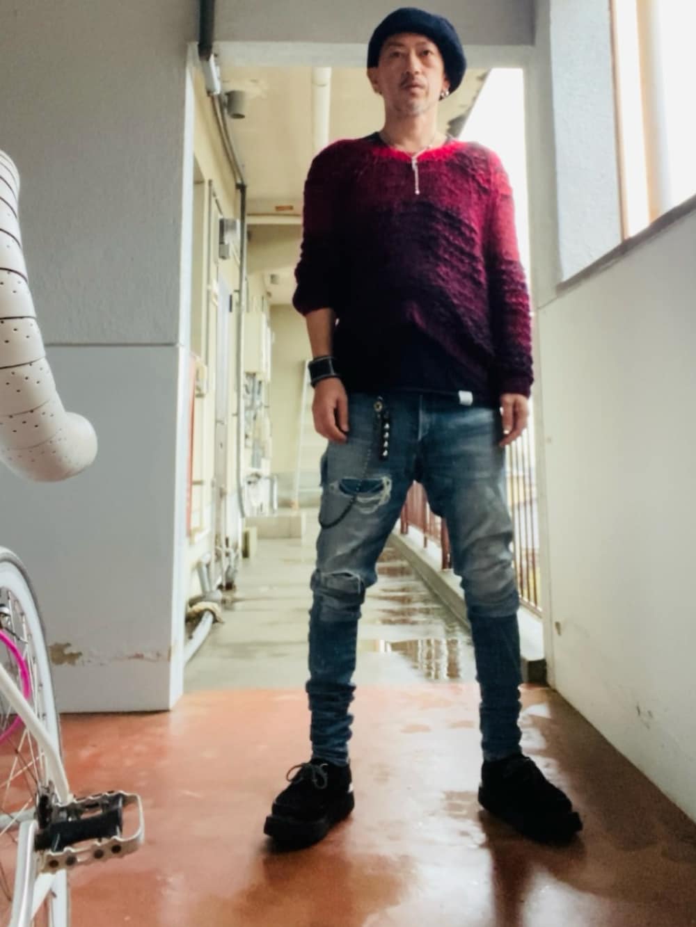 レッド系のニット/セーター、ブラック系のタンクトップ、ブルー系のデニムパンツを着用したメンズの春コーディネートの2枚目の写真