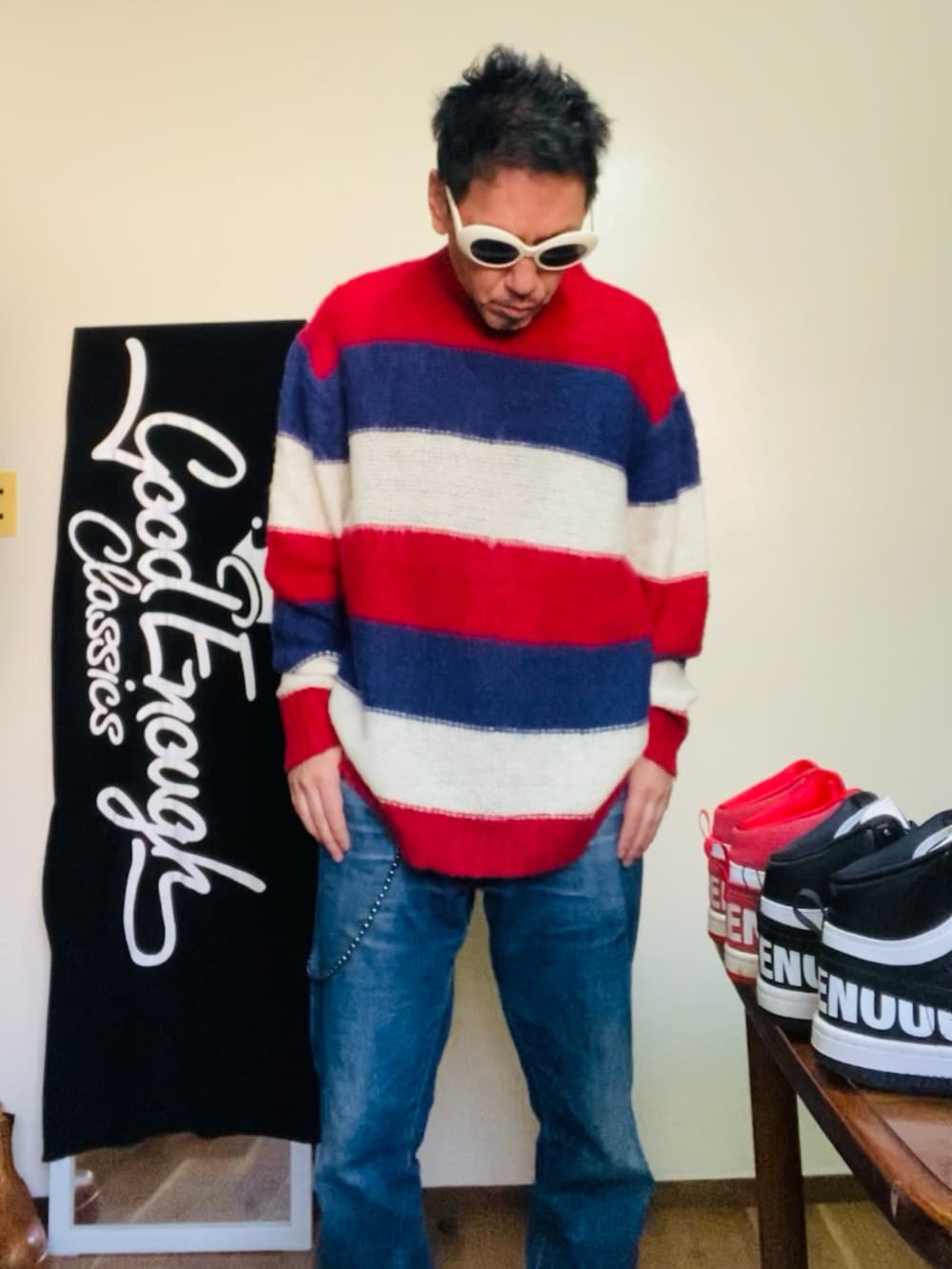 レッド系のニット/セーター、ブルー系のデニムパンツ、ベージュ系のサングラスを着用したメンズの冬コーディネートの2枚目の写真