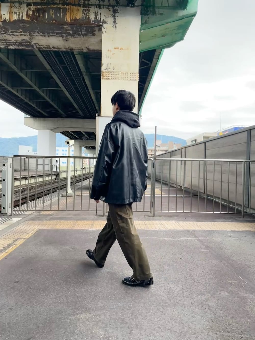 グレー系のニット/セーター、ブラック系のブルゾン、ブラウン系のチノパンツを着用したメンズの秋コーディネートの3枚目の写真