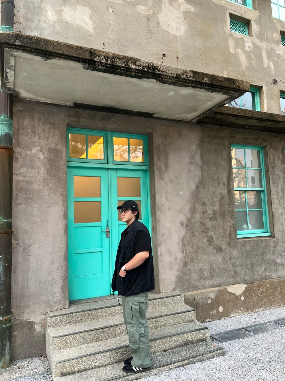 ブラック系のスニーカー、ブラック系のベスト、グリーン系のチノパンツを着用したメンズの秋コーディネートの2枚目の写真