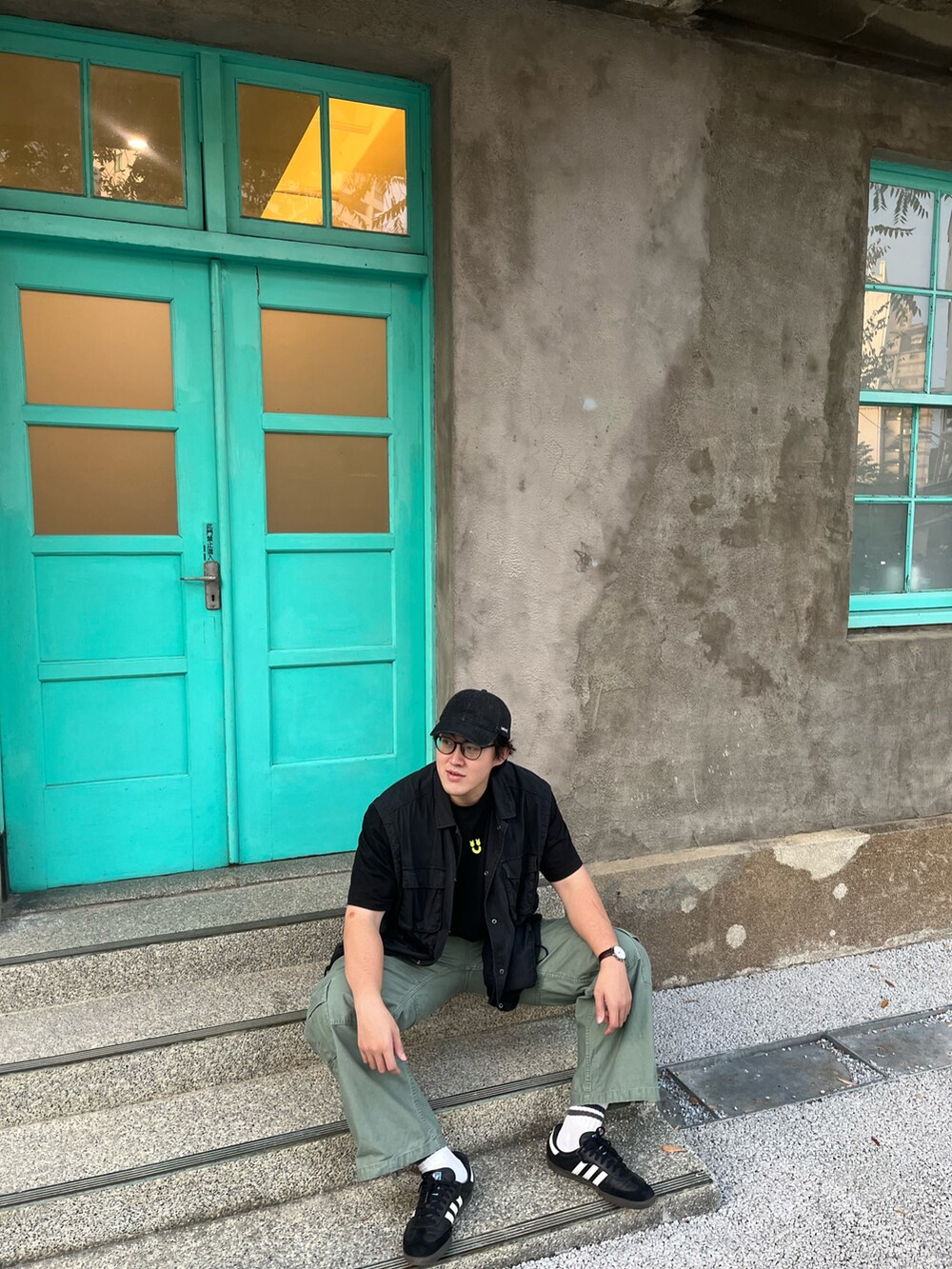 ブラック系のスニーカー、ブラック系のベスト、グリーン系のチノパンツを着用したメンズの秋コーディネートの4枚目の写真