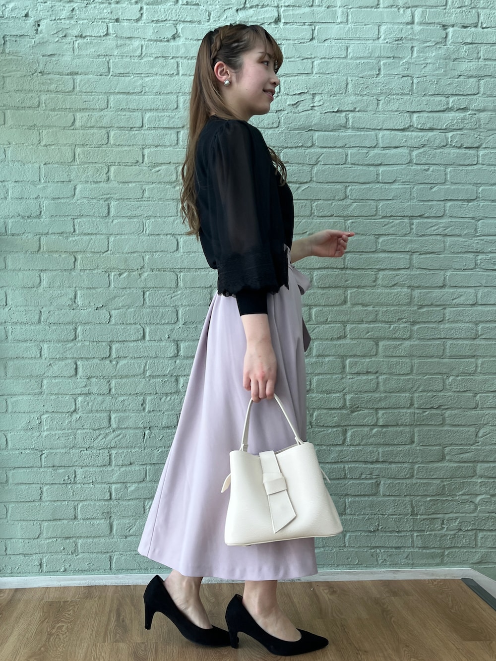 パープル系のスカート、ブラック系のニット/セーター、ブラック系のパンプスを着用したレディースの春コーディネートの2枚目の写真