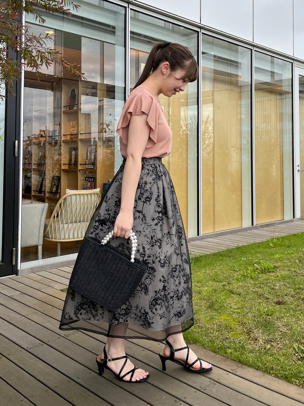 ブラック系のハンドバッグ、ブラック系のサンダル、ピンク系のニット/セーターを着用したレディースの夏コーディネートの2枚目の写真