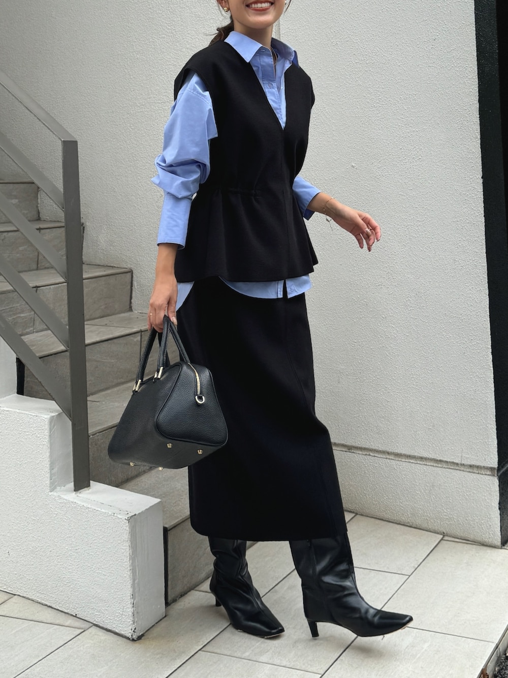 ブラック系のベスト、ブルー系のシャツ/ブラウス、ブラック系のショルダーバッグを着用したレディースの秋コーディネートの2枚目の写真
