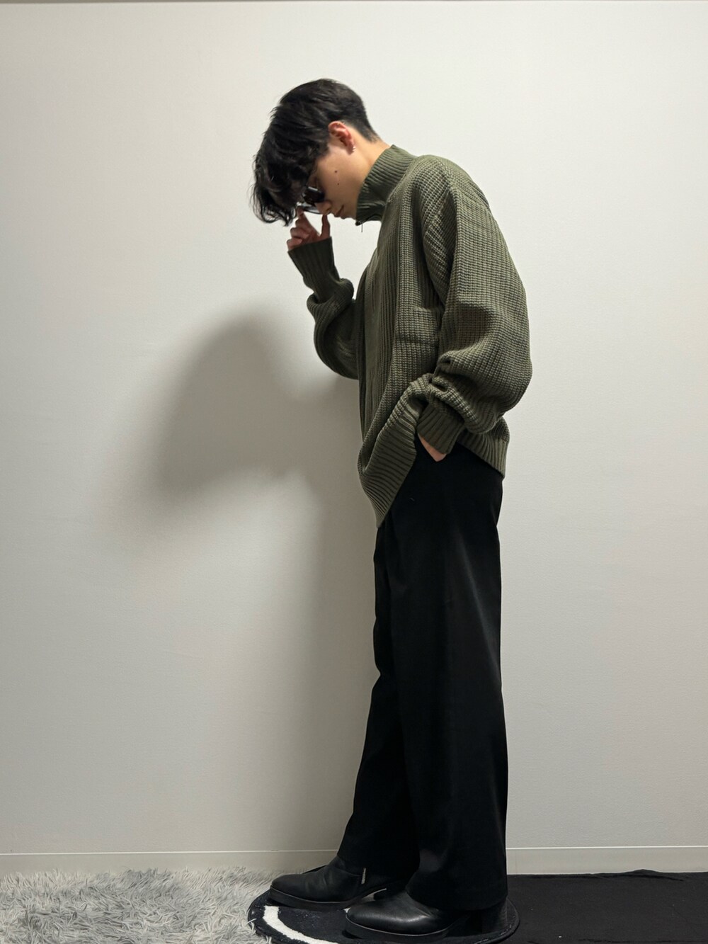 グリーン系のニット/セーター、ブラック系のスラックス、ブラック系のブーツを着用したメンズの春コーディネートの4枚目の写真