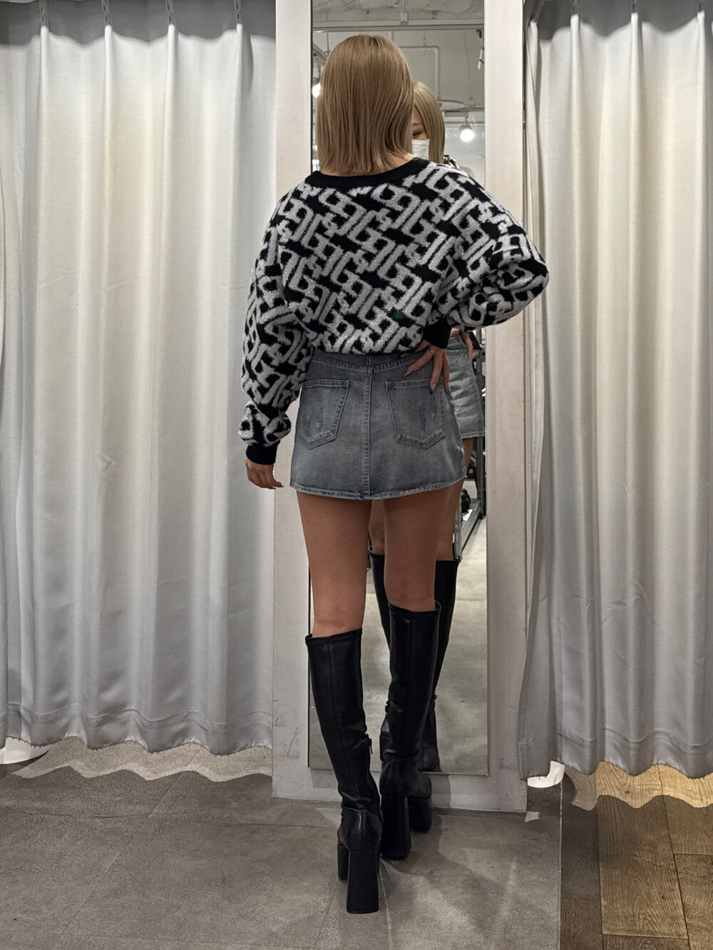 ブラック系のニット/セーター、ブルー系のデニムスカート、ブラック系のブーツを着用したレディースの冬コーディネートの2枚目の写真