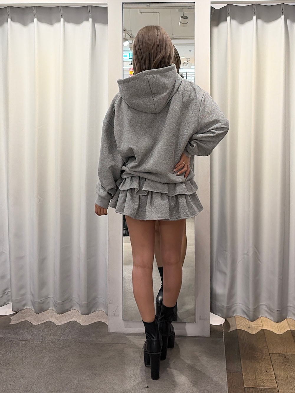 グレー系のパーカー、ブラック系のスカート、ブラック系のブーツを着用したレディースの冬コーディネートの2枚目の写真