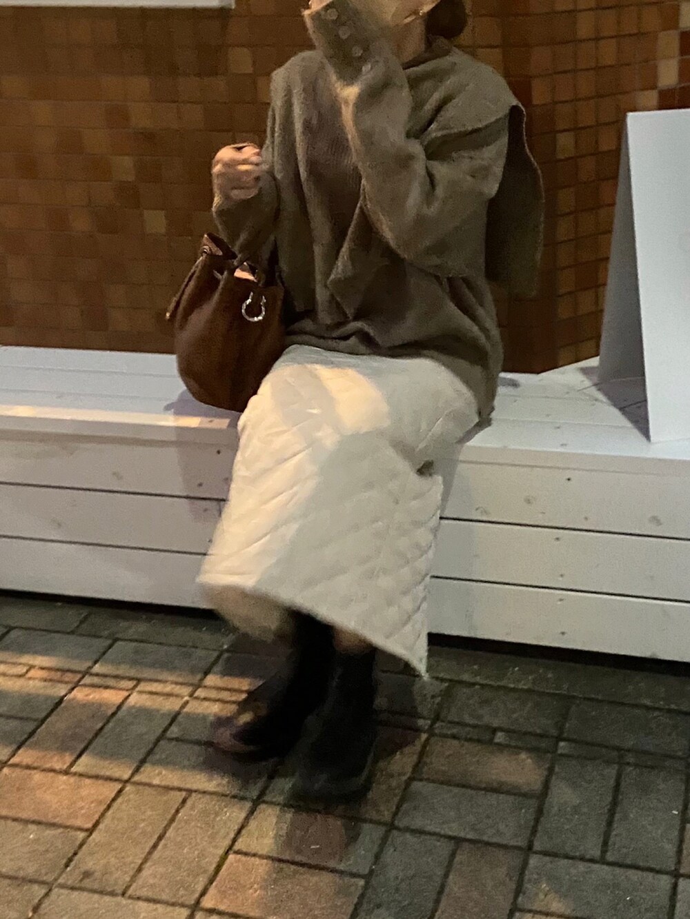 ブラウン系のニット/セーター、ホワイト系のスカート、ブラック系のブーツを着用したレディースの冬コーディネートの2枚目の写真