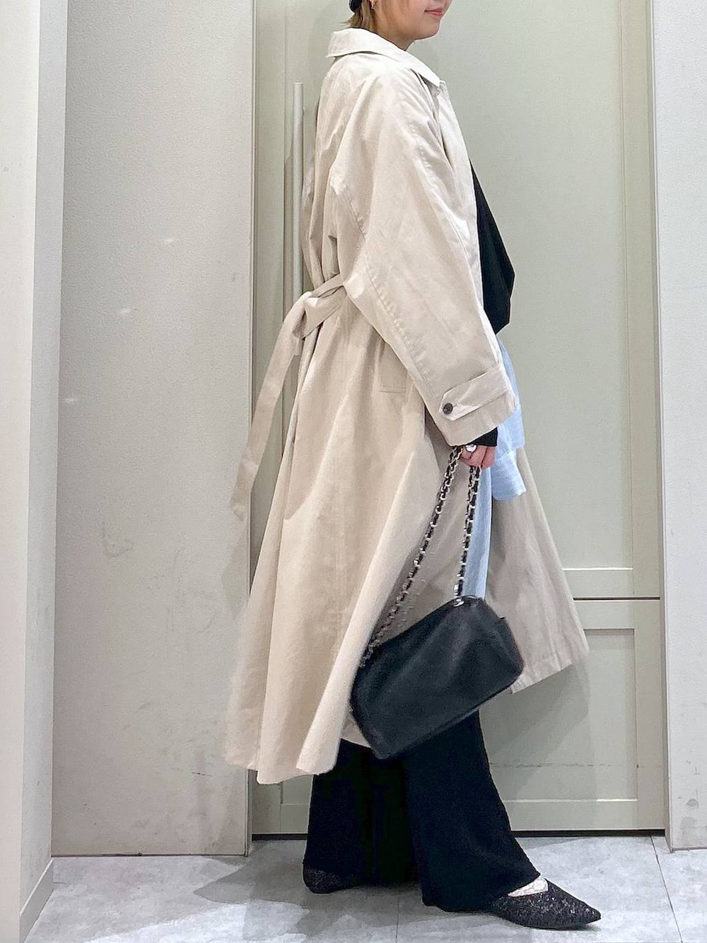 ブラック系のショルダーバッグ、ブラック系のパンプス、ベージュ系のステンカラーコートを着用したレディースの春コーディネートの5枚目の写真